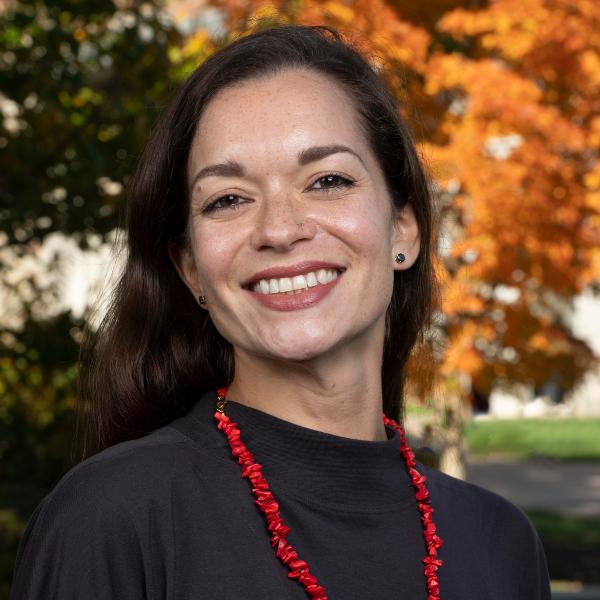 a professor wearing a black sweater and bright red necklace smiles at the camera